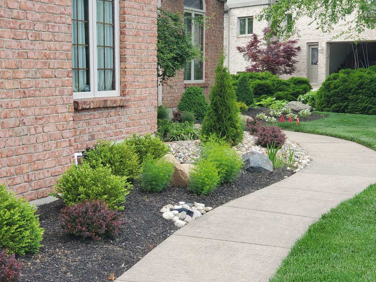 Curving front walk lined with shrubs, river rock and boulders
